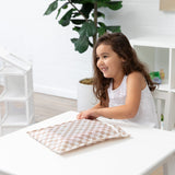A girl smiles indoors with a Roamio by Bumkins Wet Bag: Sand Check on a white table, with a plant in the background.