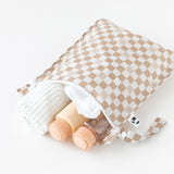 A tan Bumkins Wet Bag 2 Pack: Sand and Black Check holds a towel and bottles on a white background.