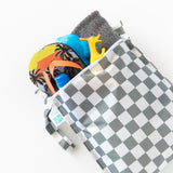The Bumkins Wet Bag + Wet/Dry Bag Set in Charcoal Check holds flip-flops, a toy giraffe, bottle, toys, and a towel.