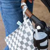 A Bumkins Wet Bag: Charcoal Check hangs on a stroller handle next to a cup holder with a drink.