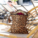 Roamio by Bumkins Wet Bag: Leopard rests on a rattan lounge chair outdoors, with clothes and a water bottle inside.