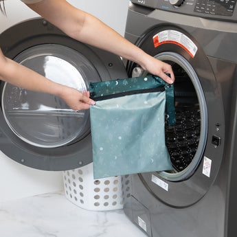 A person holds Bumkins Wet Bag: Starry Cactus in front of a front-loading washing machine.