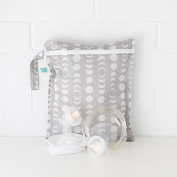 Bumkins Wet Bag: Lunar Phase is shown against a white brick background with breast pump parts in front.