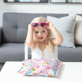 A smiling girl in a white top tries pink sunglasses at a table with the Bumkins Wet Bag + Wet/Dry Bag Set: Boots in front of her.