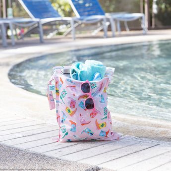 A bag from Bumkins The Playdate Planner Deluxe 5-Piece Set: Boots holds a towel, a bottle & pink sunglasses by a pool.
