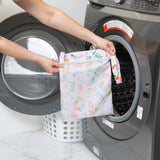 A person holds a Bumkins Wet Bag: Boots in front of an open front-loading washing machine.