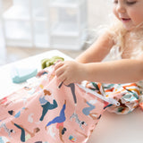 A child holds the Bumkins Yoga Pals Wet Bag + Wet/Dry Bag Set featuring women and dogs doing yoga poses.