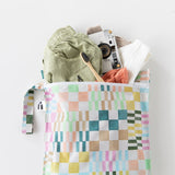 Roamio by Bumkins Wet Bag: Motley Check holds green shorts, clothes, a camera, and toothbrush on a white background.