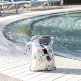 Roamio by Bumkins Wet Bag: Motley Check sits poolside, holding a towel, water bottle, camera, and sunglasses.