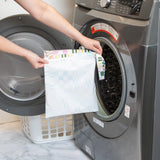 A person holds Roamio by Bumkins Wet Bag: Motley Check in front of an open front-loading washing machine.