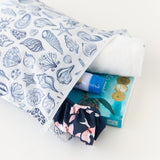 Roamio by Bumkins Wet Bag: Shells holds a towel, swimsuit, sunscreen, and book on a white background.