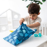 A boy eagerly opens a Bumkins Wet Bag: Blue Tropic at a white table, with a pair of blue goggles close by.