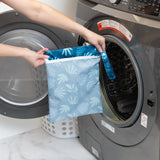 A person holds Bumkins Wet Bag: Blue Tropic in front of an open front-loading washing machine.