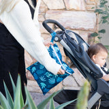 A person zips a Bumkins Wet Bag: Blue Tropic attached to a stroller with a child outdoors.
