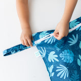 Close-up of a child zipping a Bumkins Wet Bag: Blue Tropic on a white table.