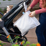 A parent attaches a Bumkins Wet Bag + Clear Travel Bag 3 Pack Set: Wander to a stroller while carrying a baby with a white bow.