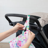 Hands attach the Bumkins Wet Bag + Wet/Dry Bag Set: Watercolor to a stroller—ideal for essentials on the go.