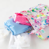 Bumkins Wet Bag + Wet/Dry Bag Set: Watercolor shown with blue/pink diapers, white cloth, and bottle on a white surface.