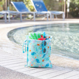 A Bumkins Wet Bag + Clear Travel Bag 3 Pack Set: Ocean Life sits poolside; empty lounge chairs are in the background.