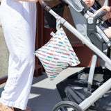 A person pushes a stroller with a baby; a Bumkins The Chaos Coordinator Deluxe 5-Piece Set: Disney Mickey & Friends Varsity on the handle.