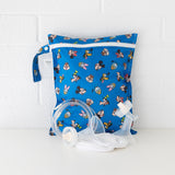 Bumkins Wet Bag: Mickey & Friends Forever sits against a white brick wall with breast pump parts in front.