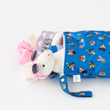 A plush toy in sunglasses peeks from a Bumkins Wet Bag: Mickey & Friends Forever, next to a pink garment and purple book on a white table.