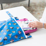 A child's hand pulls a pink tablet a the Bumkins Wet Bag: Mickey & Friends Forever on a white table.