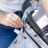 Close-up of a person attaching the Bumkins Wet Bag: No Tricks, Just Treats to a stroller handle using the snap on the strap.