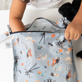 A child opening the Bumkins Wet Bag: No Tricks, Just Treats at a white table, adorned with colorful Halloween ghosts and pumpkins.