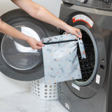 A person holds a Bumkins Wet Bag: No Tricks, Just Treats in front of a front-loading washing machine.