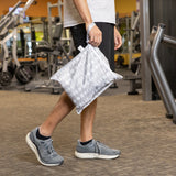 A gym-goer in athletic wear carries the Roamio by Bumkins Wet Bag 2 Pack: Desert Night past fitness equipment.