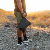 Wearing shorts and sneakers at sunset, a person holds the Roamio by Bumkins Wet Bag 2 Pack: Rich & Boujee on rocky ground.