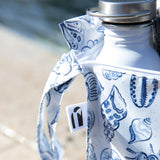 A Roamio by Bumkins Wet Bag 2 Pack: Coastal, in a blue and white seashell print, sits near the beach.