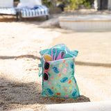 Bumkins Wet Bag 2 Pack—Ocean Life and Jungle, sits by the water, colorful and ready for beach toys and accessories.