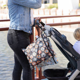 A woman strolls outdoors by a waterway with a Bumkins Wet Bag 2 Pack: Disney Everyday Is Halloween attached to her stroller.