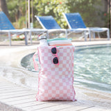 A Bumkins Wet Bag Plus 2 Pack: Mauve + Sand Check with sunglasses, towel, and water bottle sits poolside near blue lounge chairs.