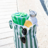 A Bumkins Wet Bag Plus 2 Pack: Green + Gray Stripe holds a towel, water bottle, sunscreen, and sunglasses by a pool.