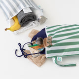 Bumkins Wet Bag Plus 2 Pack: Green + Gray Stripe holds beach essentials like a swimsuit, sunglasses, towel, & bottle on a white background.