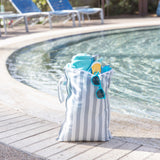A Bumkins Wet Bag Plus 2 Pack: Green + Gray Stripe sits poolside holding sunglasses, sunscreen, a towel, and more.