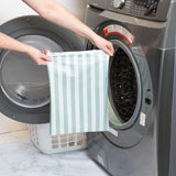 A person holds a Bumkins Wet Bag Plus 2 Pack: Green + Gray Stripe in front of an open front-loading washing machine.