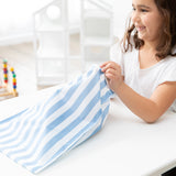 A smiling child in white shirt reaches into a Bumkins Wet Bag Plus 2 Pack: Blue + Yellow Stripe on a white table.