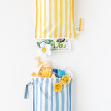 Bumkins Wet Bag Plus 2 Pack: Blue + Yellow Stripe holds baby items like stuffed toys, books, clothes, and sunglasses on a white background.