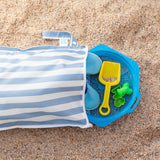 A Bumkins Wet Bag Plus 2 Pack: Blue + Yellow Stripe lays open on sand with shoes and beach toys spilling out.