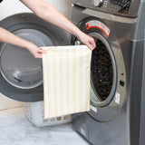 A person holds a Bumkins Wet Bag Plus 2 Pack: Blue + Yellow Stripe in front of an open front-loading washing machine.