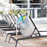 Bumkins Extra Large Wet Bag: Charcoal Check hangs on a poolside lounge chair with sunglasses and swimwear; nearby are chairs and umbrellas.