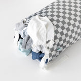 Bumkins Extra Large Wet Bag: Charcoal Check with clothes spilling out, including a white top and blue jeans, on a white background.