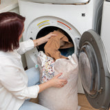 A person loading clothes into a front-loading washing machine from a Bumkins Extra Large Wet Bag: Wander.