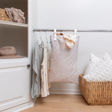 A closet with clothes, a basket of pillows, blankets on a shelf, and Bumkins Extra Large Wet Bag: Wander hanging next to clothes on a rack.
