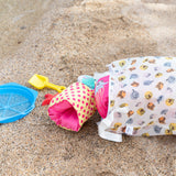 Beach toys lay scattered near a Bumkins Extra Large Wet Bag: Winnie + Friends lying on the sand.