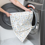 A person places a Bumkins Extra Large Wet Bag: Winnie + Friends into an open front-loading washing machine.
